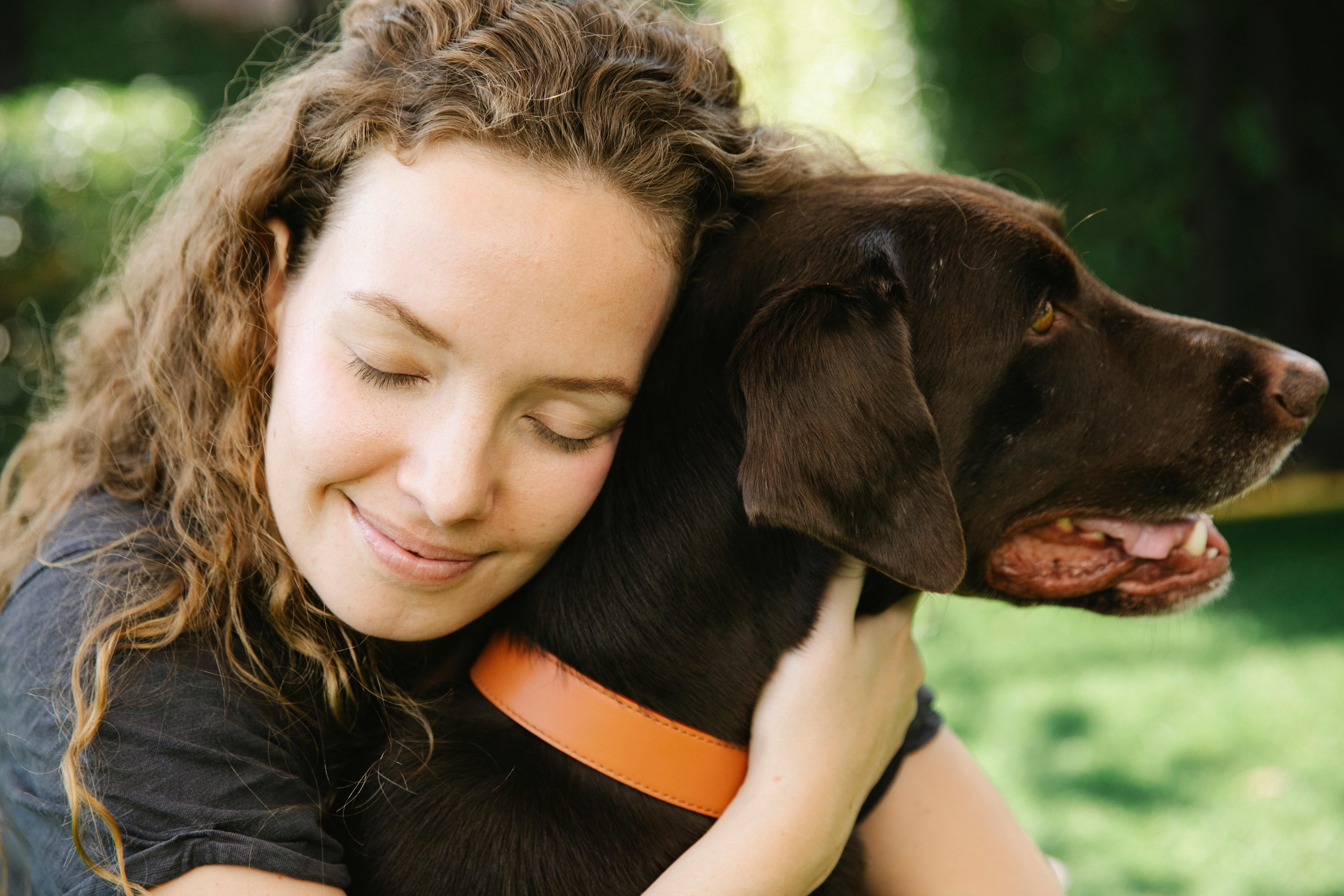 Woman embracing dog on lawn. Photo by Blue Bird